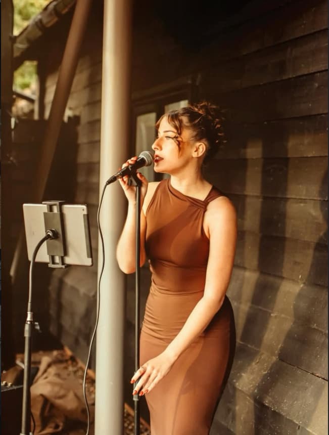 Singing outdoors at golden hour — microphone, iPad stand, wooden cabin wall