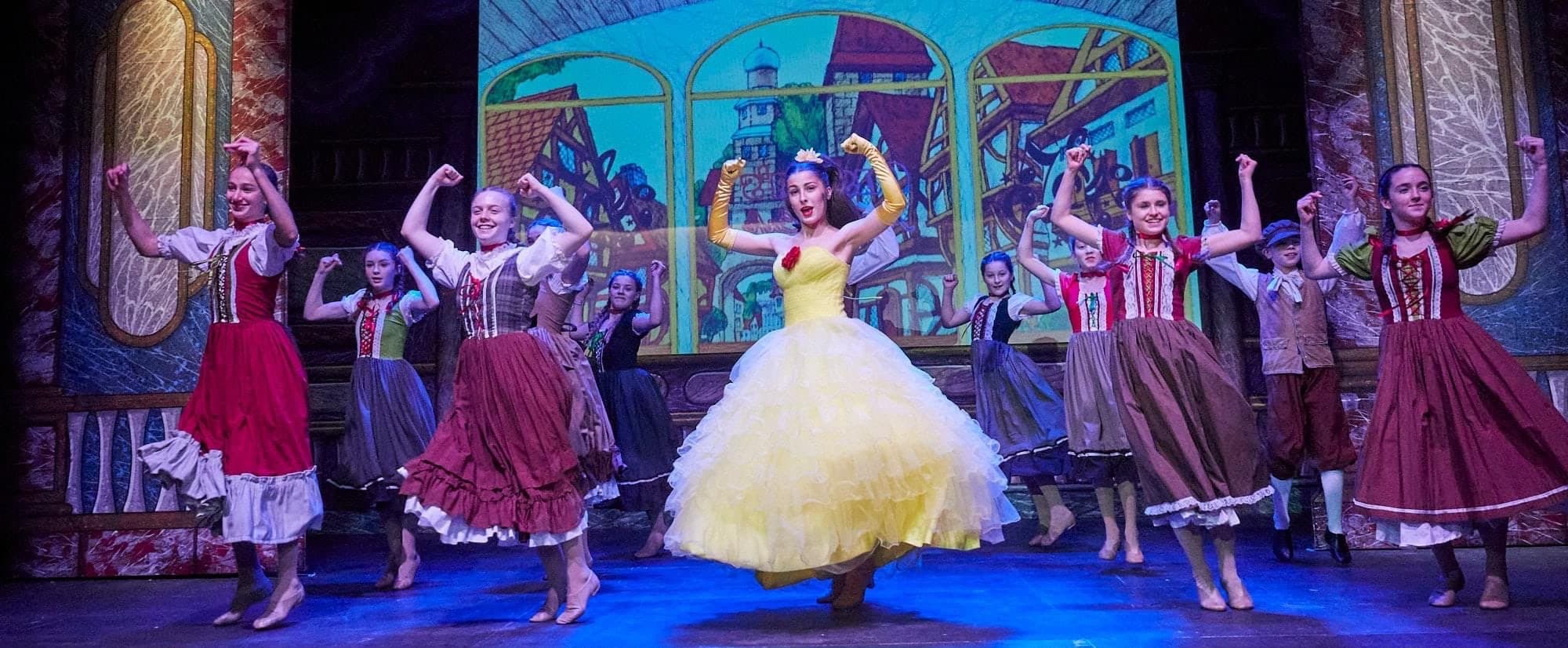 Centre stage as Belle in Beauty and the Beast — yellow gown, village ensemble, painted backdrop